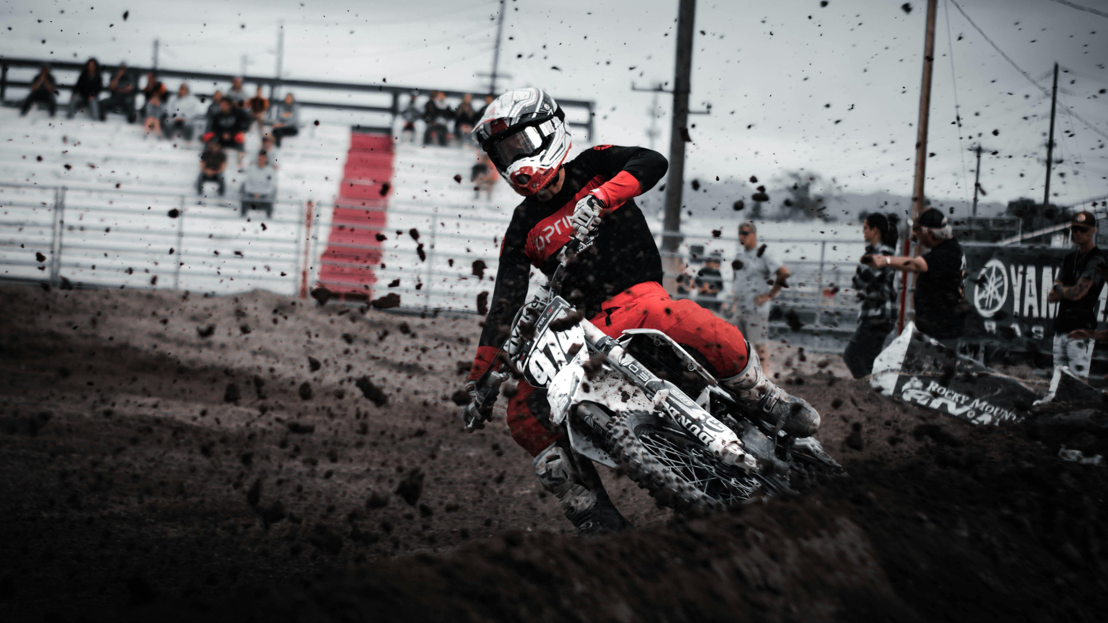Motocross rider in action on a dirt track with spectators and Yamaha branding in the background.